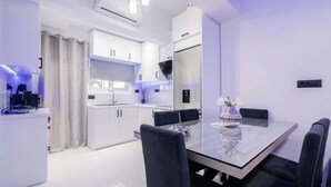 Une cuisine moderne avec des meubles blancs, un four encastré et un coin repas comprenant une table en verre et des chaises noires.