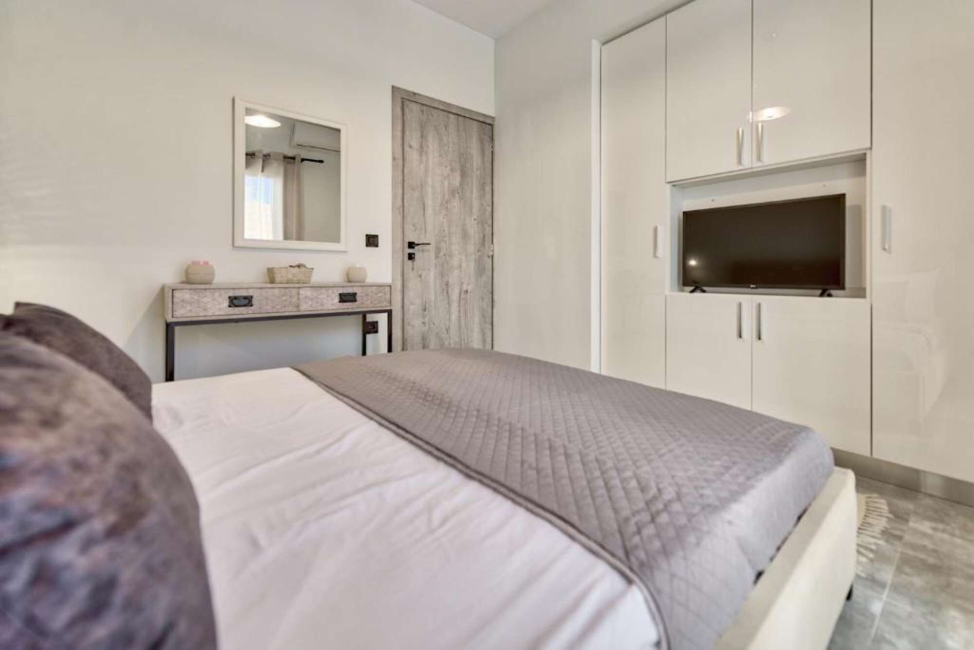 A bedroom with a bed, a vanity with a mirror, a wardrobe, and a television.