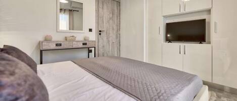 A bedroom with a bed, a vanity with a mirror, a wardrobe, and a television.