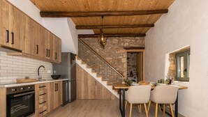 Une cuisine avec des meubles en bois, un mur en pierre, un escalier et un coin repas avec des chaises.