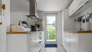 Een smalle keuken met witte kastjes, een houten aanrechtblad en uitzicht door een glazen deur naar buiten.