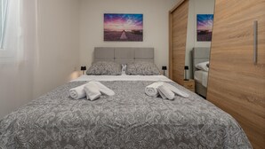A neatly made bed with patterned bedding, two pillows, and two rolled towels.