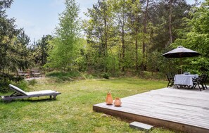 A wooden deck with a table and chairs, surrounded by a grassy area and trees. - 3 bedroom gorgeous home in Højby (Højby)