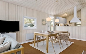 A cozy living room with a TV, a dining area with a table and chairs, and a kitchen visible through an open door.