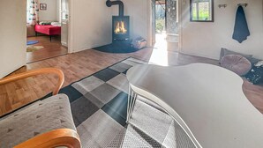 A modern living room with a large white sofa, a wooden chair, a black and white patterned rug, a stone fireplace, and a view of the outdoors through a glass door.