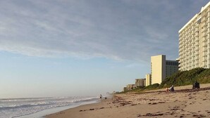 A beach with a sandy shore, a few people, and a large hotel building in the background. - Charming Coastal Escape (Melbourne)