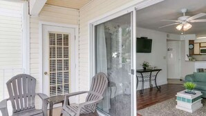 A room with a sliding glass door, a ceiling fan, a small table with a plant, and a green couch. - Charming Coastal Escape (Melbourne)