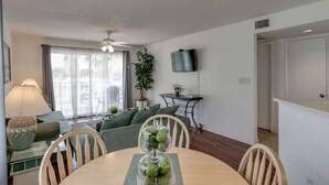 A living room with a sofa, a dining table with chairs, a TV mounted on the wall, and a ceiling fan. - Charming Coastal Escape (Melbourne)