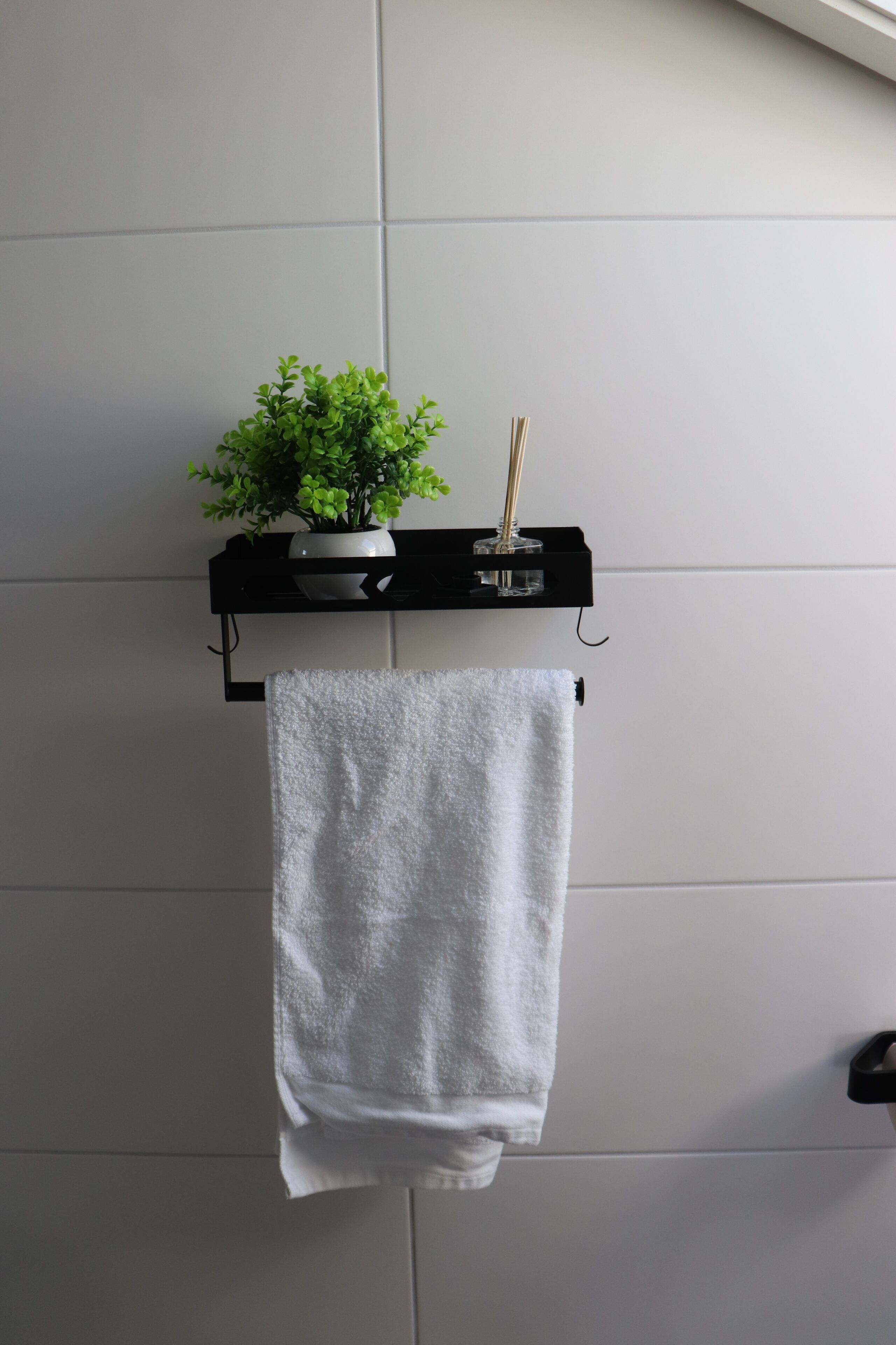 Ein Badezimmer mit einem weißen Handtuch an einem schwarzen Handtuchhalter, einer Topfpflanze und einer Handseifenflasche.