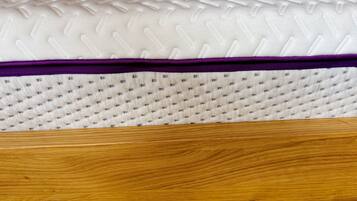 A mattress with a textured top and a purple edge, placed on a wooden bed frame.