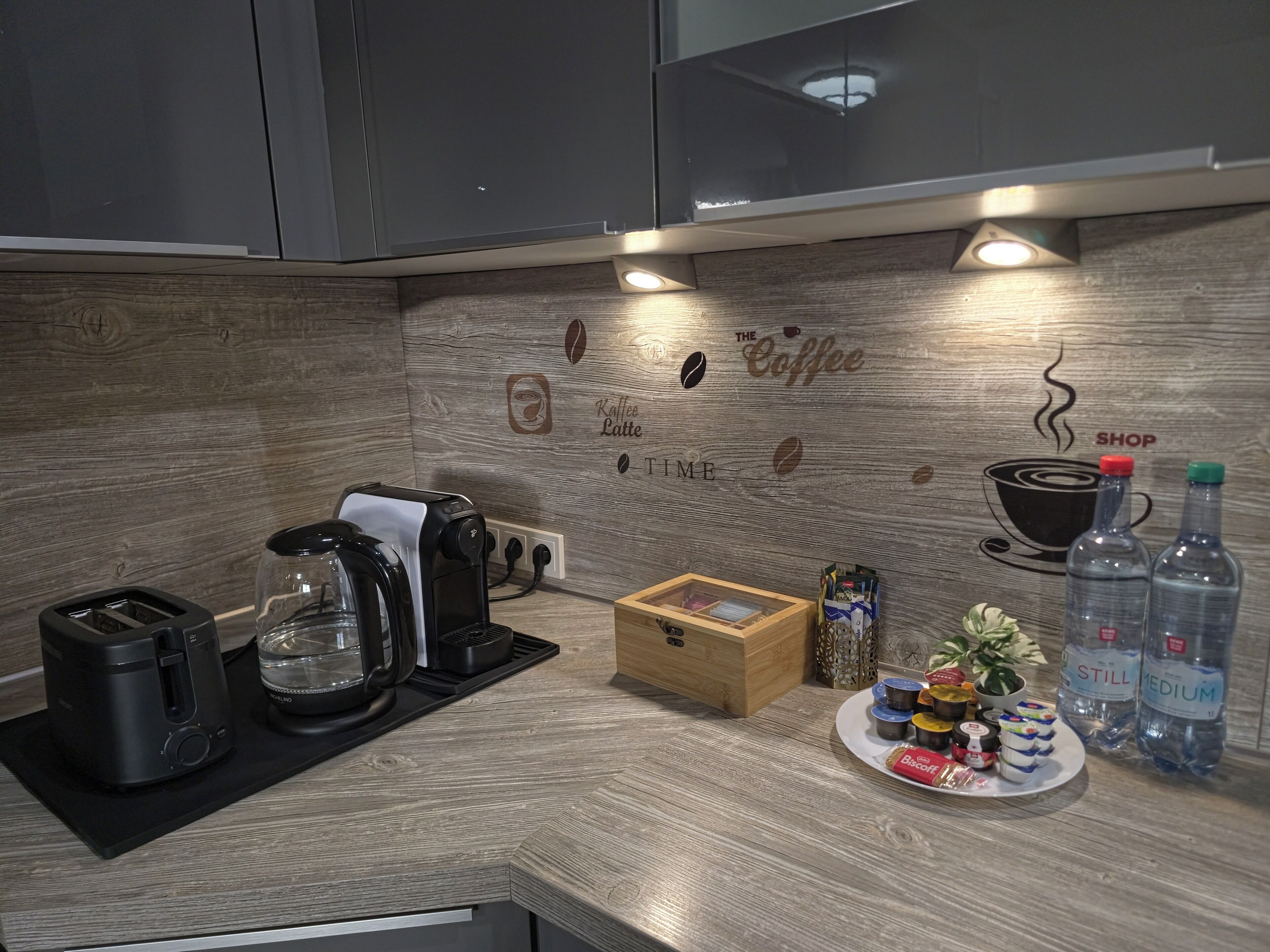 A modern kitchen with a coffee-themed backsplash, a coffee machine, a toaster, and a plate of pastries.