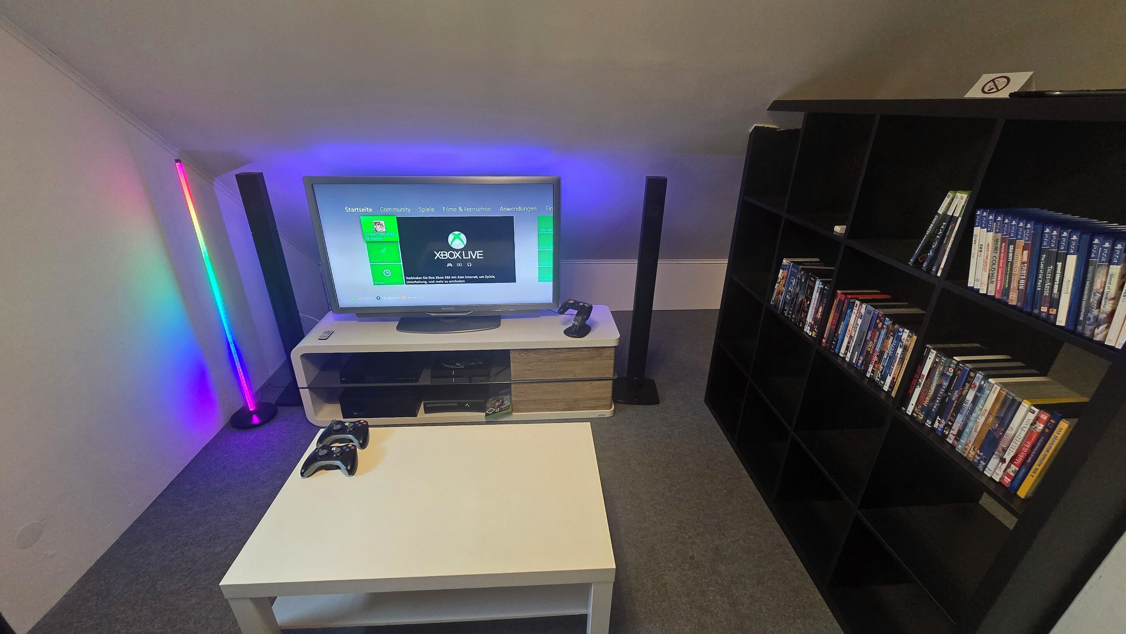 A room with a TV on a stand, a gaming console, a bookshelf, and a desk.