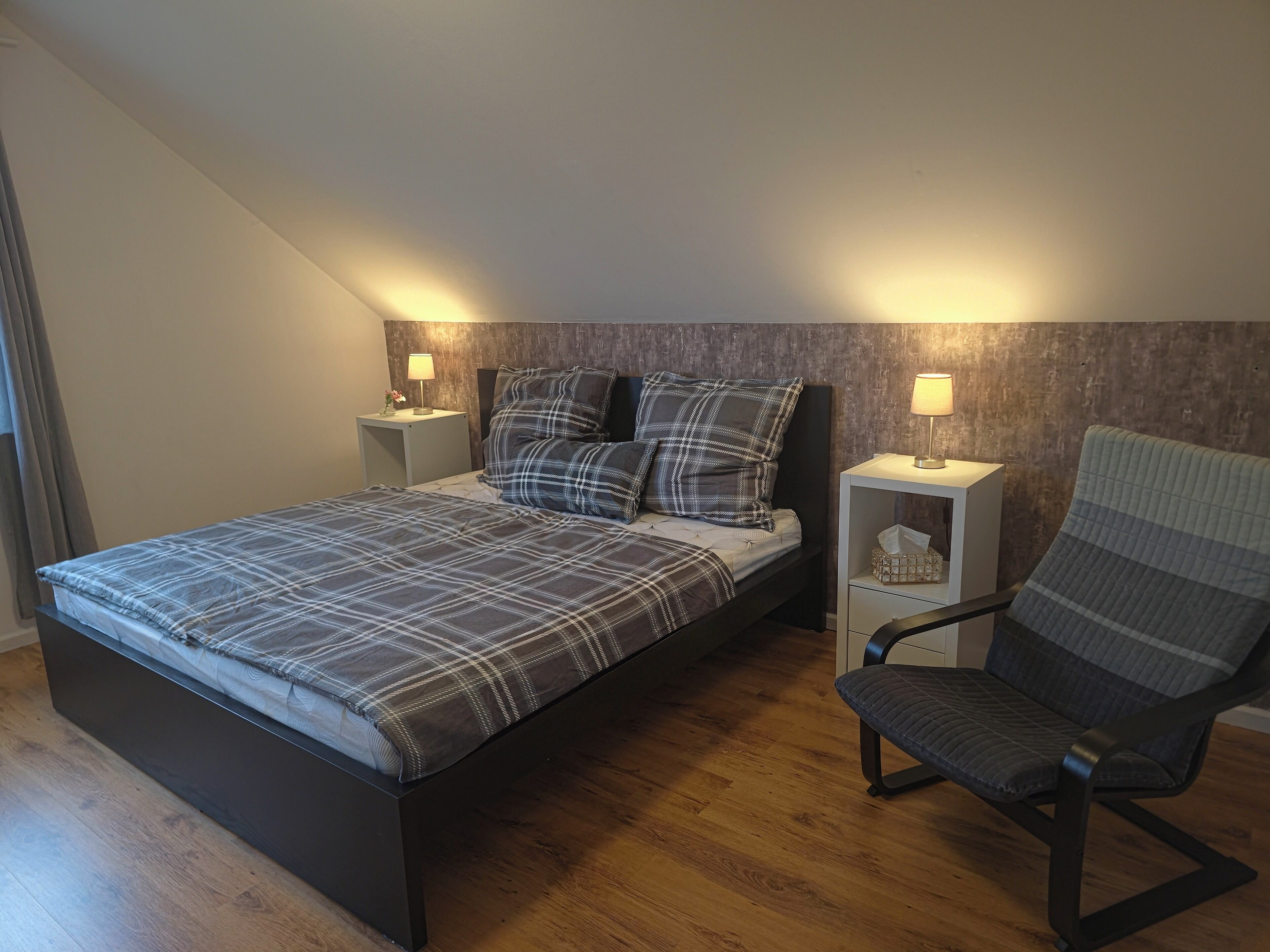 Une chambre à coucher avec un lit, deux tables de chevet avec des lampes, une chaise et un plancher en bois.