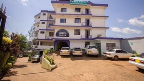 A multi-story hotel with a sign reading "DANS HOTEL" and "HOTEL DADOS" on the facade. There are several cars parked in front, and the building has multiple balconies. - Dan's Hotel Kisii (Kisii)