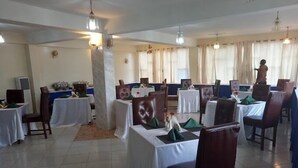 A dining area with tables set for service, a person standing near the back, and a tiled floor. - Dan's Hotel Kisii (Kisii)