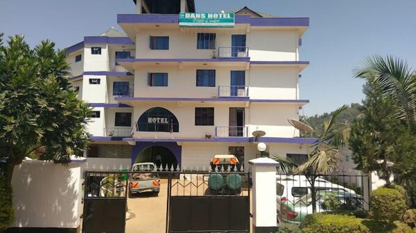 A multi-story hotel with a prominent entrance gate, a sign reading "DANS HOTEL," and a clear view of the parking area with several vehicles.
