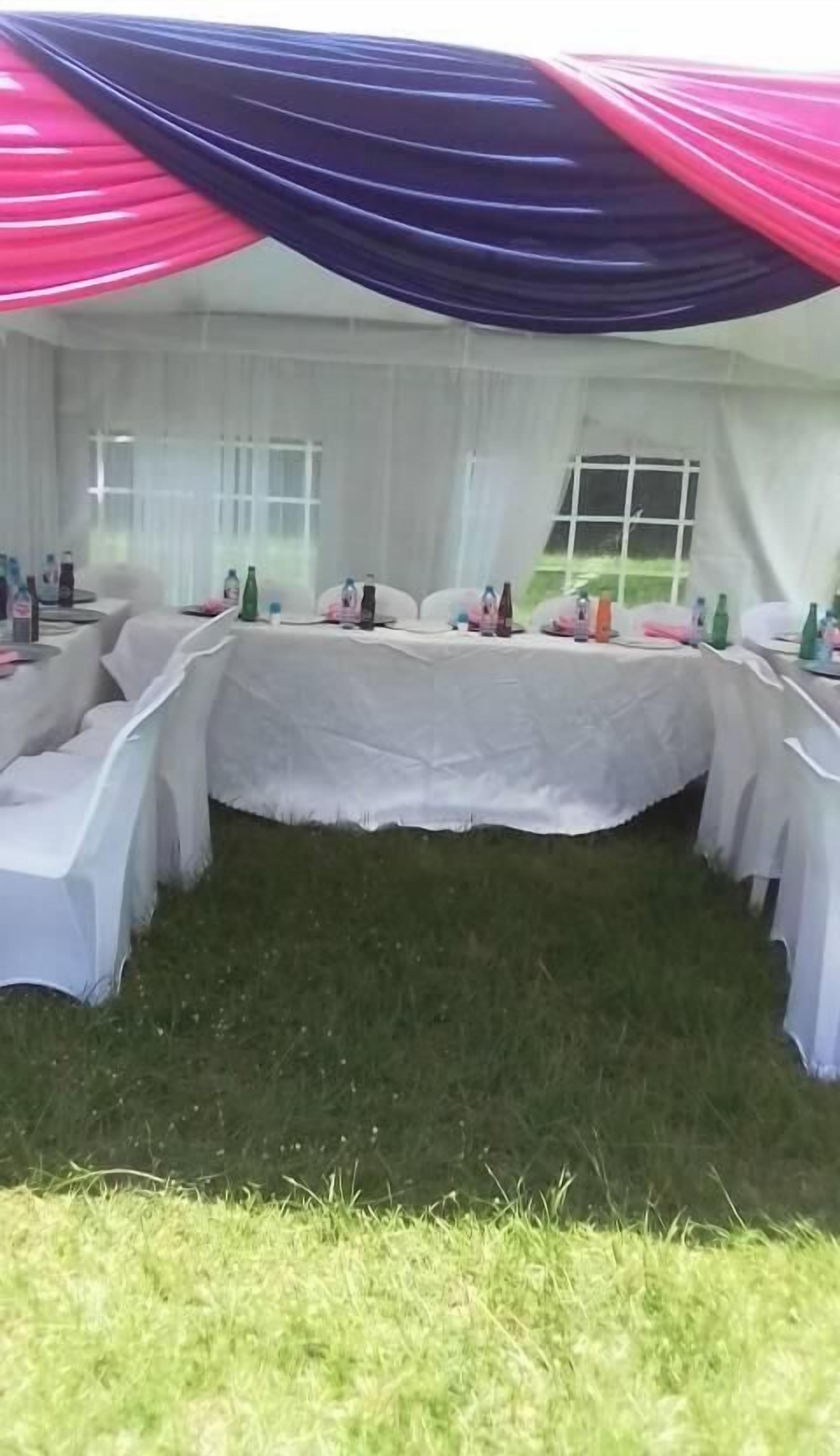 A tented outdoor event space with tables set up for dining, covered with white tablecloths and featuring various table settings.