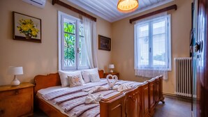 Een slaapkamer met een houten bed, twee nachtkastjes, een radiator en een raam met gordijnen.