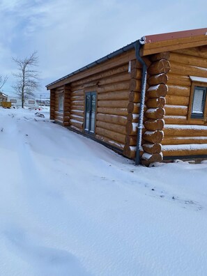 Une cabane en rondins avec une fenêtre et une porte, entourée de neige.