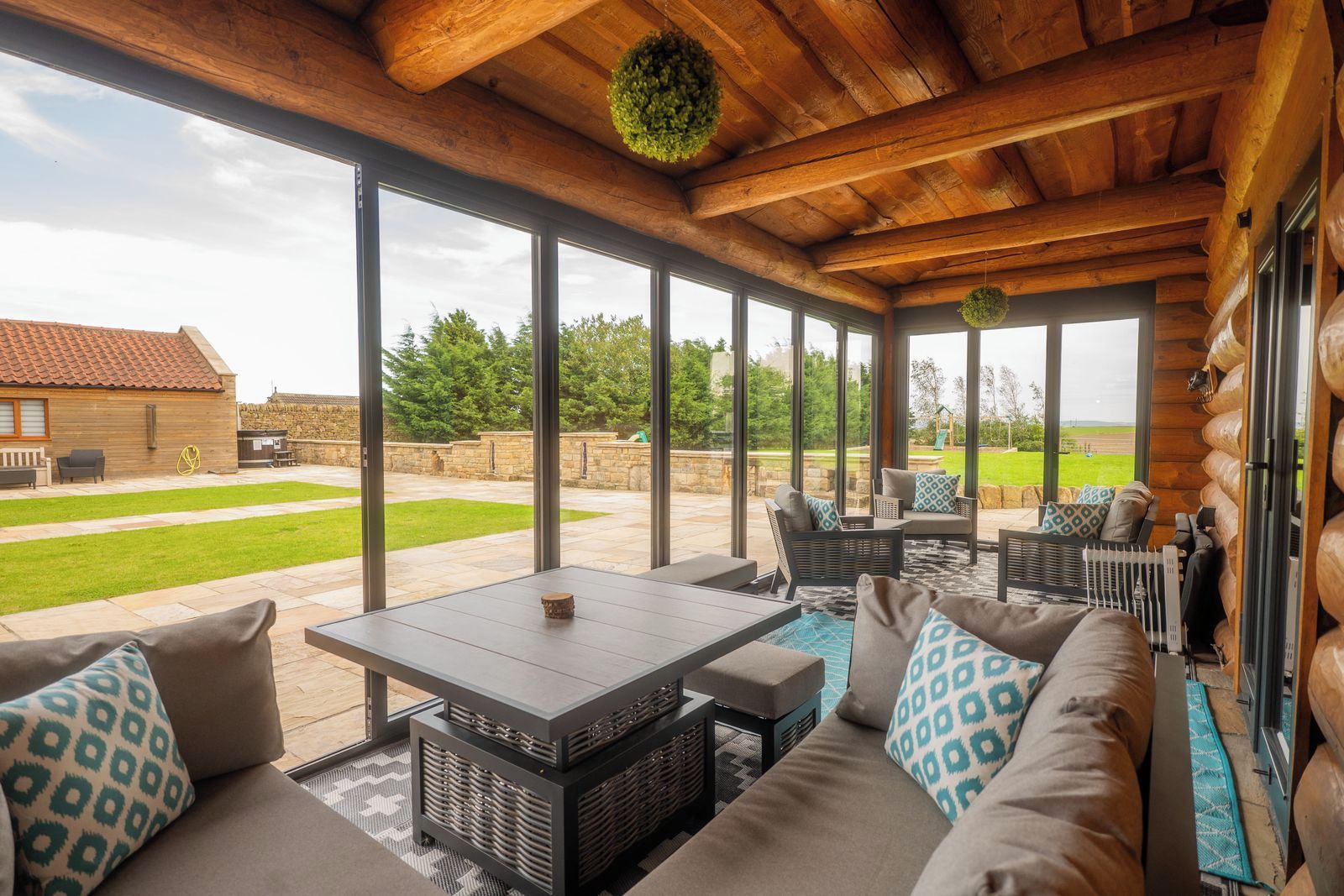 A covered outdoor seating area with a table and chairs, large windows, and a view of the backyard.