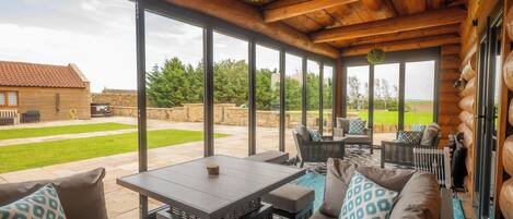 A covered outdoor seating area with a table and chairs, large windows, and a view of the backyard.