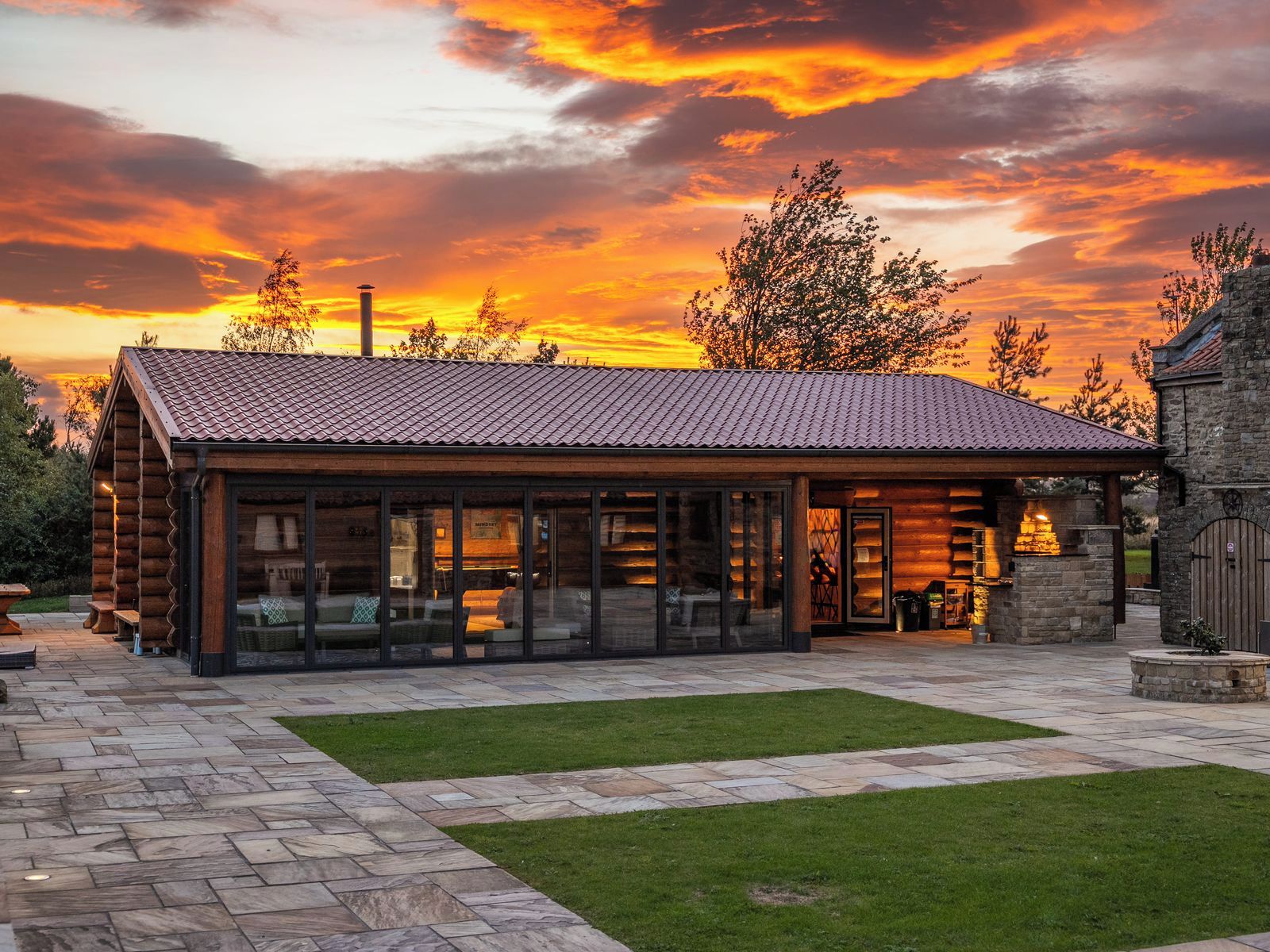 A log cabin with a tiled roof, large glass windows, and a stone pathway leading to the entrance.