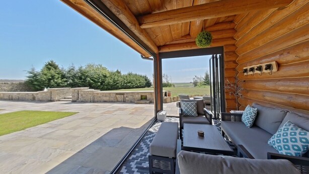 Una cabaña de madera con un patio amueblado con asientos exteriores y vistas al campo.