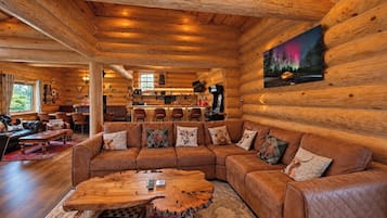 A log cabin interior with a large wooden sofa, a unique coffee table, and a painting of a forest scene.