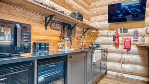 Una cocina moderna con horno empotrado, cafetera y microondas. Hay una pared de madera con un televisor montado y un cartel que dice "By Order of the Peaky Blindfrys".