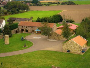 Un bâtiment en pierre surmonté d’un toit de tuiles rouges, entouré d’une pelouse bien entretenue et d’une allée circulaire.