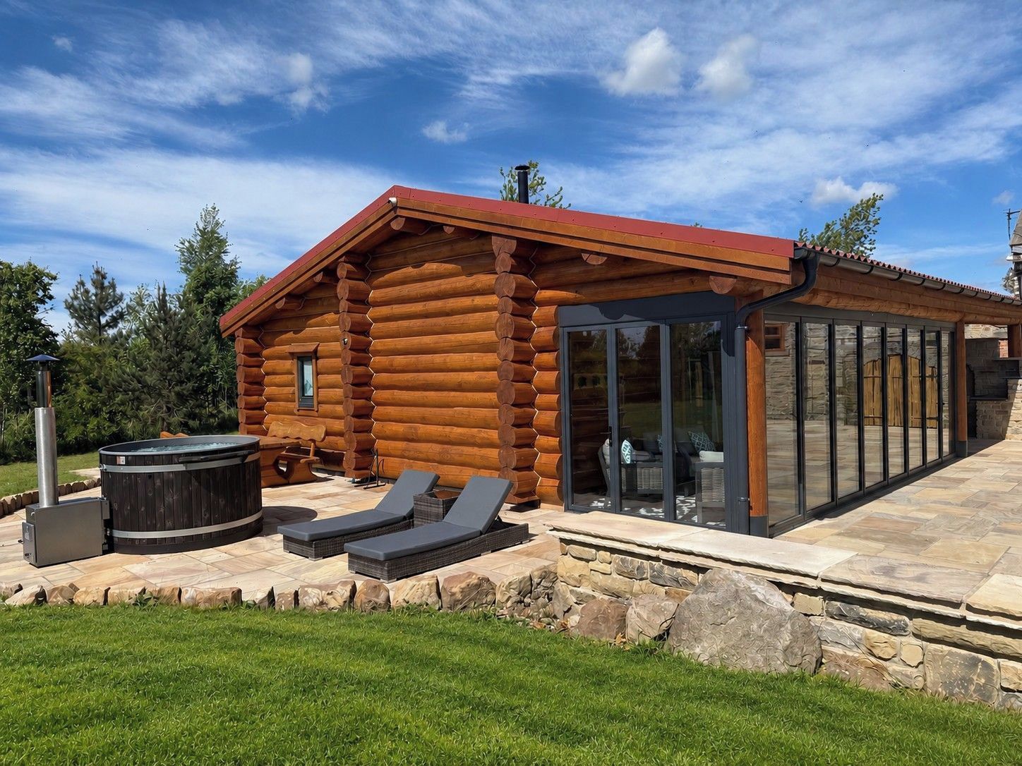A log cabin with a glass-enclosed patio, outdoor seating, and a hot tub.