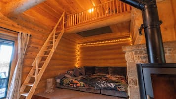 A cozy cabin interior with a wooden staircase, a fireplace, and a window overlooking a snowy landscape.