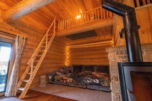 L’intérieur chaleureux d’un chalet avec un escalier en bois, une cheminée et une fenêtre donnant sur un paysage enneigé.