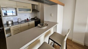 Una cocina moderna con microondas, tostadora, hervidor y estufa. El techo es de madera y la encimera, blanca.