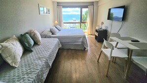 Habitación de hotel con dos camas, un escritorio, una silla, televisión y balcón con vistas al mar.