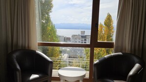 Una habitación con dos sillones de cuero y una mesita redonda, un ventanal con vistas al agua y edificios.