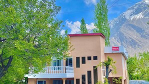 A two-story building with a balcony, a red roof, and a mountain backdrop. - Spacious 9-bedroom hotel suites in beautiful Skardu with WiFi (Skardu)