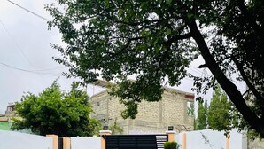 A paved driveway leading to a gated entrance with a brick wall and a tree providing shade. - Spacious 9-bedroom hotel suites in beautiful Skardu with WiFi (Skardu)