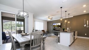 A modern kitchen with a dining area, featuring a wooden dining table, chairs, pendant lights, and a built-in island with a sink. - Storey Lake Resort, Private Pool, Near Famous Attractions!! (Kissimmee)