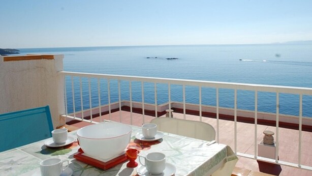 Un balcón con una mesa lista para comer, con vista a un mar tranquilo.