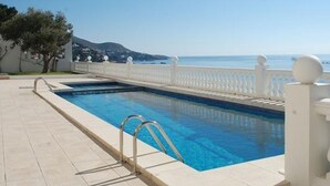 Una piscina rectangular con cerca blanca y balaustradas, rodeada de una solana con baldosas.