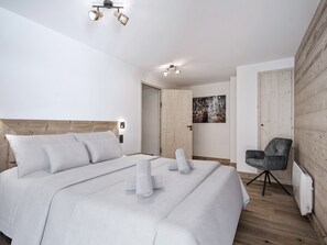 Un dormitorio moderno con una cama grande, cabecera de madera, lámpara de pared, una puerta y un cuadro enmarcado.