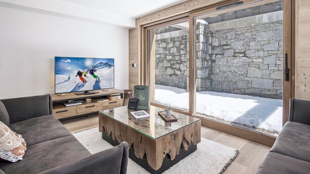Ein modernes Wohnzimmer mit großem Fernseher, einem Holztisch und grauen Sofas.
