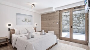 Ein modernes Schlafzimmer mit einem großen Bett, einer Holzwand, einer Steinwand und einer Glastür, die zu einem verschneiten Außenbereich führt.