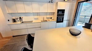 A modern kitchen with white cabinetry, a built-in oven, and a dining area with a white table and black bowl.