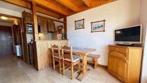 A wooden interior with a dining table, chairs, a television, and kitchen cabinets.