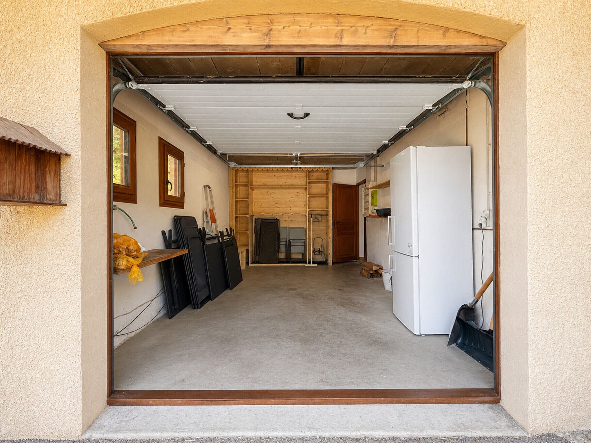 A garage with a white refrigerator, a wooden door, and a concrete floor.