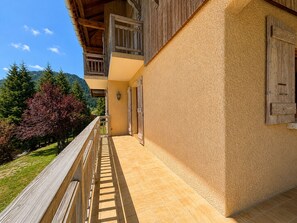 A building with a balcony, wooden shutters, and a view of trees and mountains.