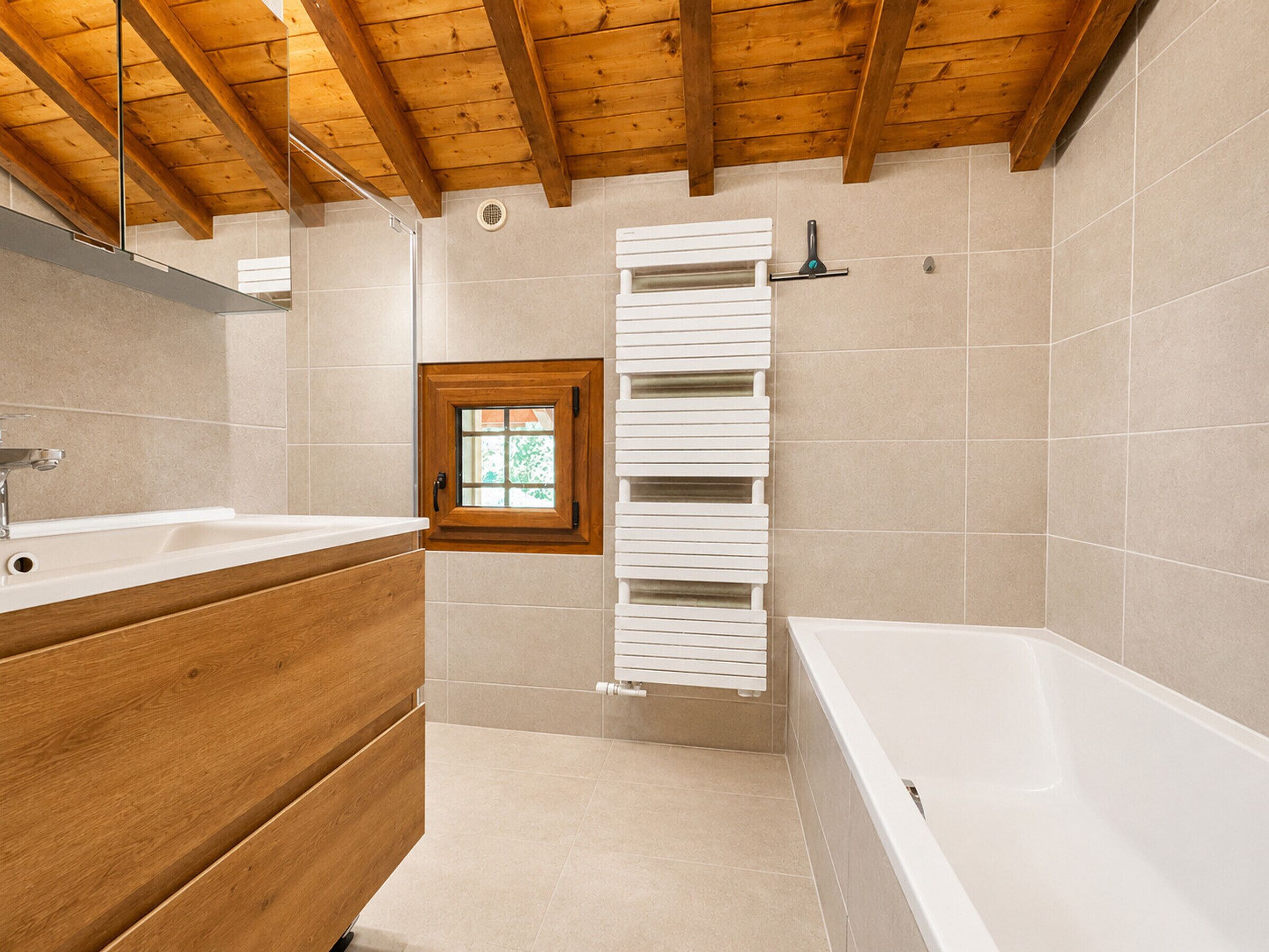 A bathroom with a wooden ceiling, a bathtub, a sink, and a window.