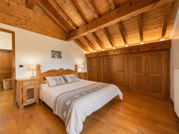 A bedroom with a wooden ceiling, a bed with a headboard, bedside tables, and a wardrobe.